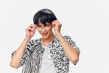 Young man wearing round glasses adjusting them while smiling, dressed in a black and white patterned shirt with short sleeves, isolated on white background.