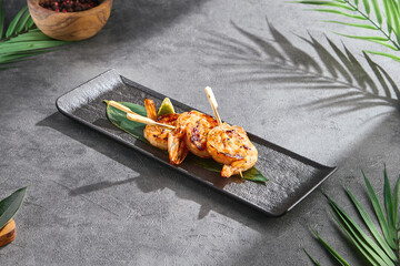 Shrimp yakitori skewers in bright lighting, elegant overhead composition on black rectangular plate