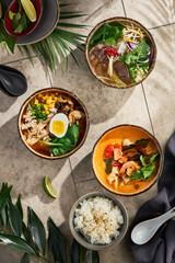 Tom yum, pho bo, and ramen soups with rice in rustic, bright overhead composition