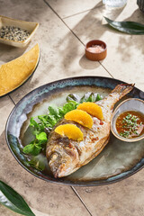 Whole dorado with orange slices, moody natural lighting, overhead ceramic plate composition