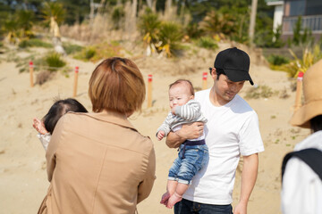 In early March, Japanese families enjoy the beach together: a 6-month-old baby, a 1-year-old girl, a 3-year-old girl, and parents in their 30s. A cheerful springtime scene filled with warmth and joy.