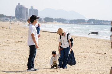 In early March, a 6-month-old baby, a 3-year-old girl, and their Japanese parents in their 30s walk together on a sandy beach by the sea. A springtime moment filled with warmth and connection.