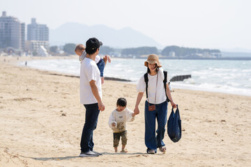 In early March, a 6-month-old baby, a 3-year-old girl, and their Japanese parents in their 30s walk together on a sandy beach by the sea. A springtime moment filled with warmth and connection.
