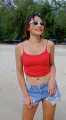 Pretty Asian woman rocking denim shorts and a red top stands confidently on a tropical beach