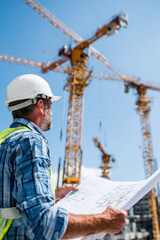 Engineer inspecting a construction site with cranes and blueprints