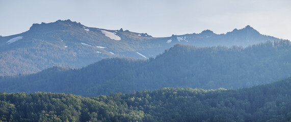 Mountain peaks covered with forests and snow, evening light, panoramic view