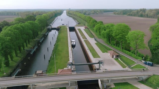 Semi orbit movement showing a barge entering Doerpen Lock, with structured canal design and parallel tree lines under soft daylight.