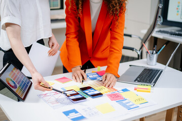 Closeup of UX UI designers planning mobile layouts with wireframes, color swatches, sticky notes,...