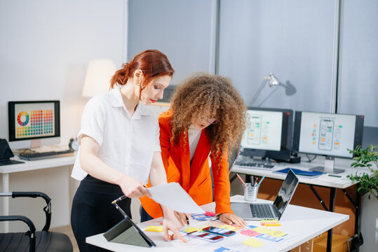Two female designers brainstorming color palettes in a modern office. Creative teamwork, branding, and UI UX