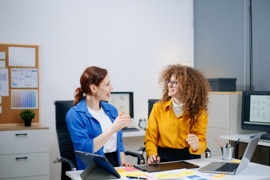 Two women discussing mobile app wireframes in a modern office. UX UI team collaboration, design thinking, and creative planning.