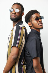 Confident black men wearing stylish sunglasses stand back-to-back, showcasing their unique fashion...