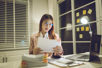 Professional young woman wearing glasses and blazer working with her laptop at a tidy desk,...