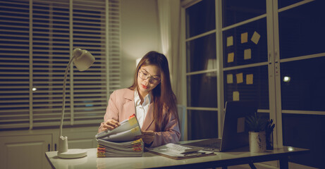 Professional young woman wearing glasses and blazer working with her laptop at a tidy desk,...