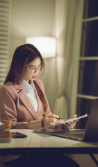 Professional young woman wearing glasses and blazer working with her laptop at a tidy desk,...