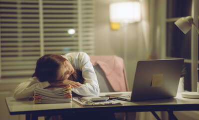 A tired woman stretches at her desk during late-night remote work, balancing stress and...