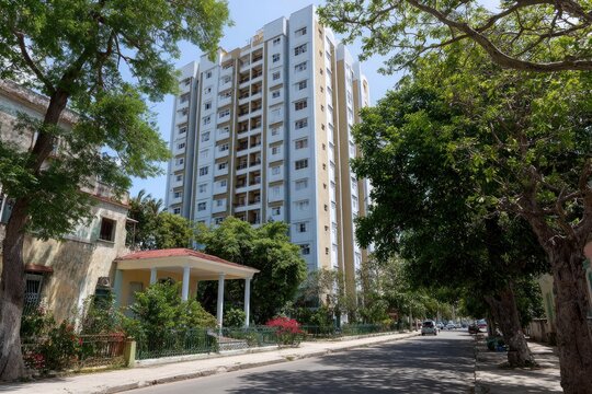 Tall apartment building amidst lush trees old home street and cars on a sunny day