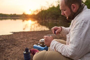 Traveler grinding coffee beans in his portable grinder for breakfast outdoors at dawn, in El Palmar...