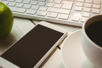 Flat design graphic is showing white smartphone on wood desk with keyboard, coffee cup, green apple