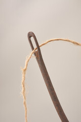close-up of coarse coconut coir thread through eye of old rusty sack needle isolated neutral gray background, natural and industrial material concept