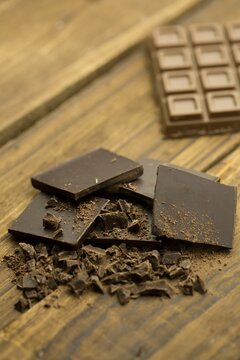Naklejki Dark chocolate squares with broken shards lying on wooden tabletop, showing segmented chocolate bar