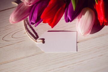 Tulip cluster is casting soft shadows on wooden tabletop in flat design, with blank gift tag