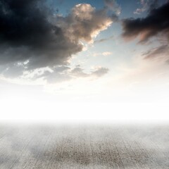 Textured concrete floor is stretching toward horizon beneath sky blending dark clouds with light