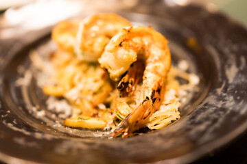 A grilled shrimp spaghetti dish garnished, served on a dark plate