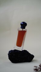 A luxury glass perfume bottle with cap containing  liquid lies on gray background, sprig of flowers...