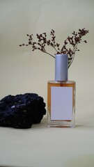 A luxury glass perfume bottle with cap containing  liquid lies on gray background, sprig of flowers...