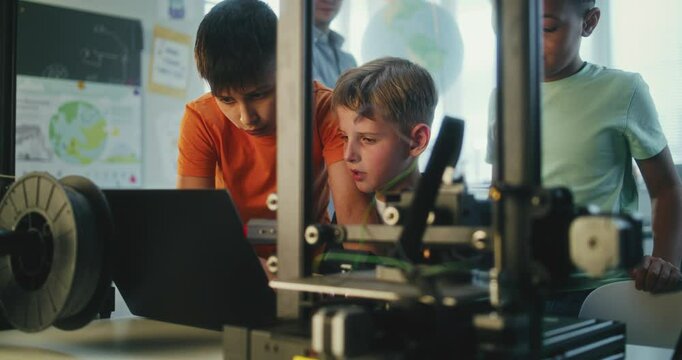 Elementary School Students Writing Code for Advanced Automated 3D Printer on Laptop During Programming Lesson. Smart Young Boys Studying in Group in Multicultural Classroom. Interactive STEM Education