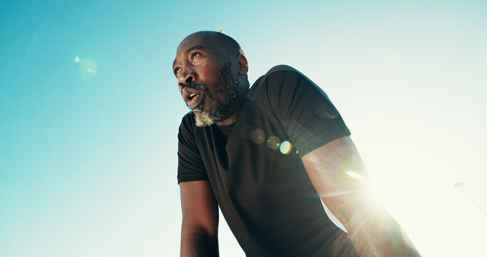 Breathing, fitness and black man by blue sky for running, workout or training for marathon with break. Fatigue, lens flare and African mature athlete with rest for outdoor cardio exercise from below.