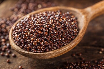 A wooden spoon filled with dark quinoa seeds set on a wooden surface with scattered quinoa around it