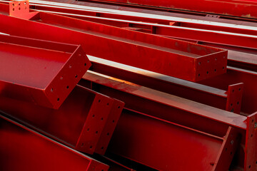 Stack of red steel beams with drill holes in close-up view