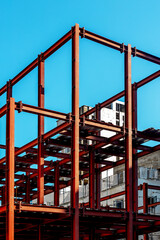 Red steel framework of urban construction site against clear blue sky