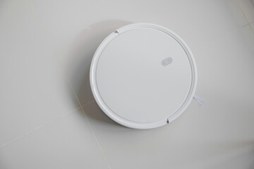 White automatic floor cleaner with side brush on tile flooring. Top view of robot vacuum cleaner...