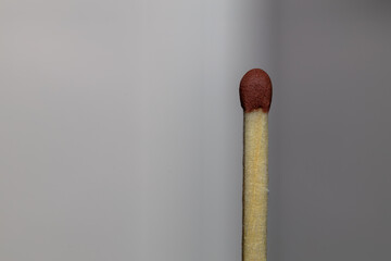 Detailed view of an unlit matchstick with a red tip on a gray background.