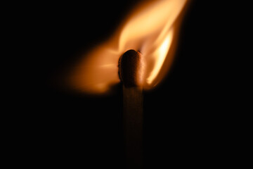 Close-up of a matchstick igniting with vibrant flame and dark contrasting background.