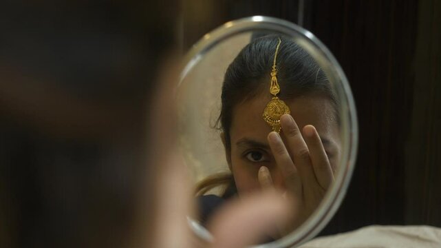 Young and beautiful south asian woman wearing gold jewellery while looking at mirror, Closeup