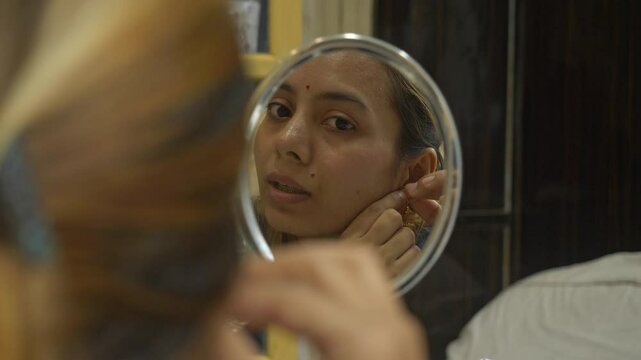 Young and beautiful south asian woman wearing gold earrings while looking at mirror, Closeup
