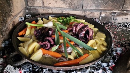 Octopus with vegetables slowly cooking under traditional iron bell lid