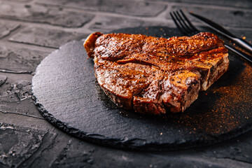 T-bone grilled beef steak with spices on black serving plate