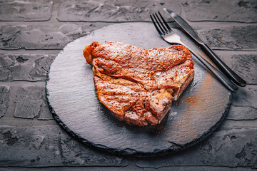 T-bone grilled beef steak with spices on black serving plate