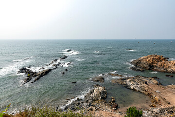 Rocky Coastline and Boats on Calm Ocean Under Clear Sky – Anjuna Beach, Goa