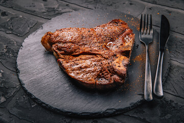 T-bone grilled beef steak with spices on black serving plate