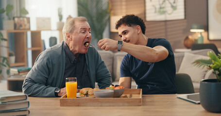 Home, caregiver and feed senior man in retirement for nutrition, assistance and lunch meal. Assisted living, nurse and helping old person with eating in lounge for rehabilitation and homecare service