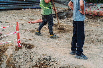 City infrastructure repair scene with open roads, red polypropylene pipes, construction workers, and excavation equipment. Urban utilities and roadwork maintenance in progress