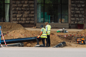 City infrastructure repair scene with open roads, red polypropylene pipes, construction workers, and excavation equipment. Urban utilities and roadwork maintenance in progress