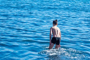 Teen boy playing in ocean waves on black volcanic sand beach, joyful summer moment, natural fun,...