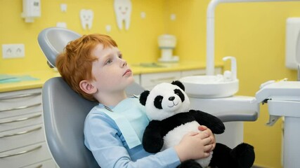 Red-haired boy with toy panda in dental chair, pediatric dentistry anxiety relief