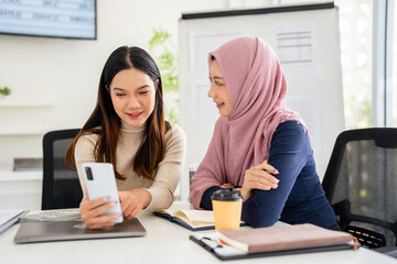 Happy diverse colleagues browsing social media content during working day in office. female partners discussing cellular application while connecting to internet